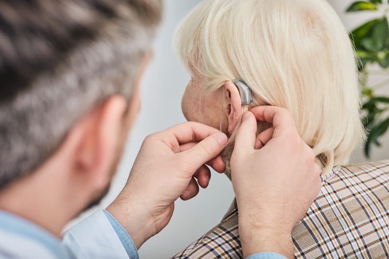 Audiologist fitting woman with hearing aids.