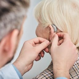 Audiologist fitting woman with hearing aids.