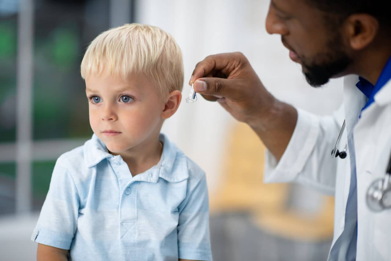 A doctor fits a little boy for a hearing aid.
