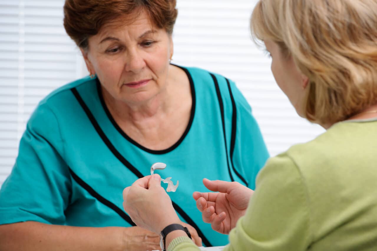 Audiologist explaining how hearing aids work to a female patient.