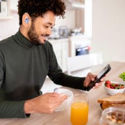 Young man with hearing aids looking at his smartphone over breakfast.