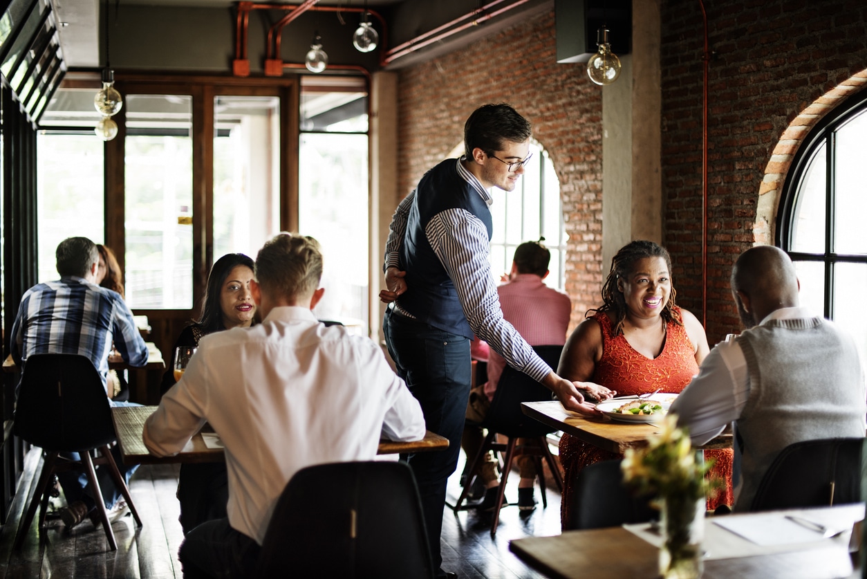 Photo of multiple tables in a restaurant, lots of people talking and eating.