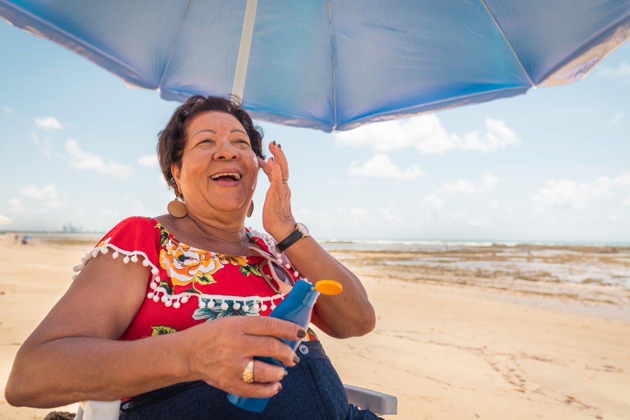 Happy woman putting sunscreen on at the beach.