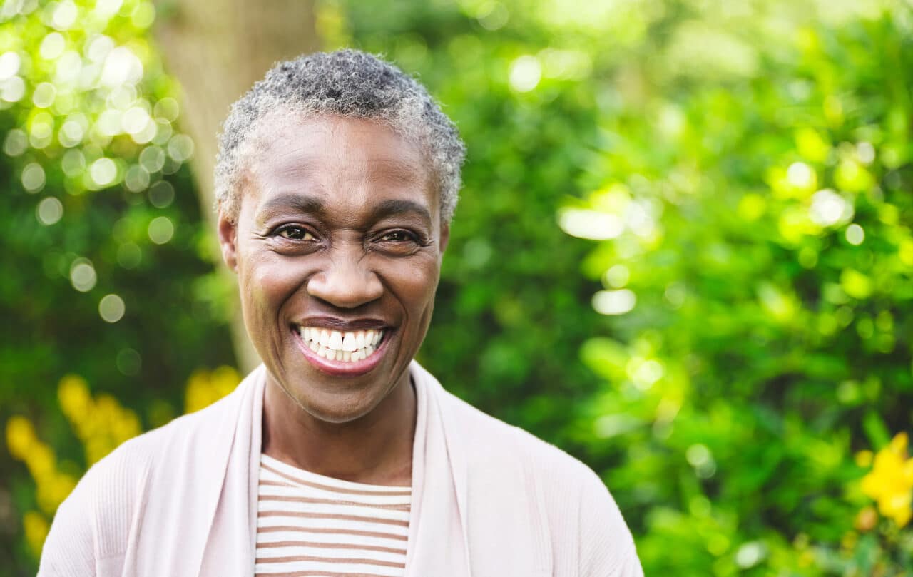 Smiling senior woman against tree background.