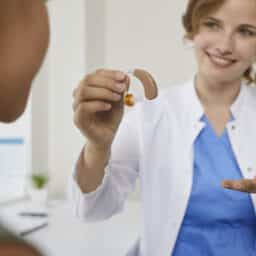 Smiling audiologist gives a modern hearing aid to a patient